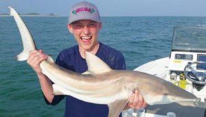 Saltwater fishing, boy holding small shark on boat