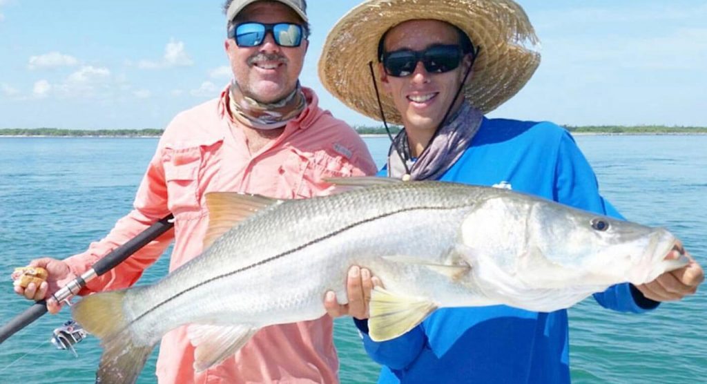 Orlando's best guided fishing charter, two men holding snook fish with bright blue ocean background