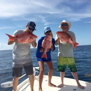 Port Canaveral group of three friends holding red, large caught fish on bow of boat