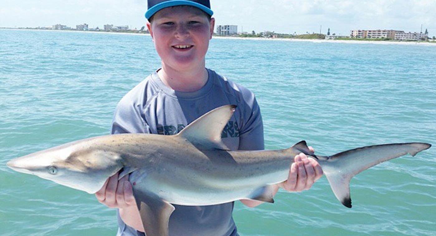 Young angler holding a small shark on a Fin & Fly shark fishing charter off Cocoa Beach